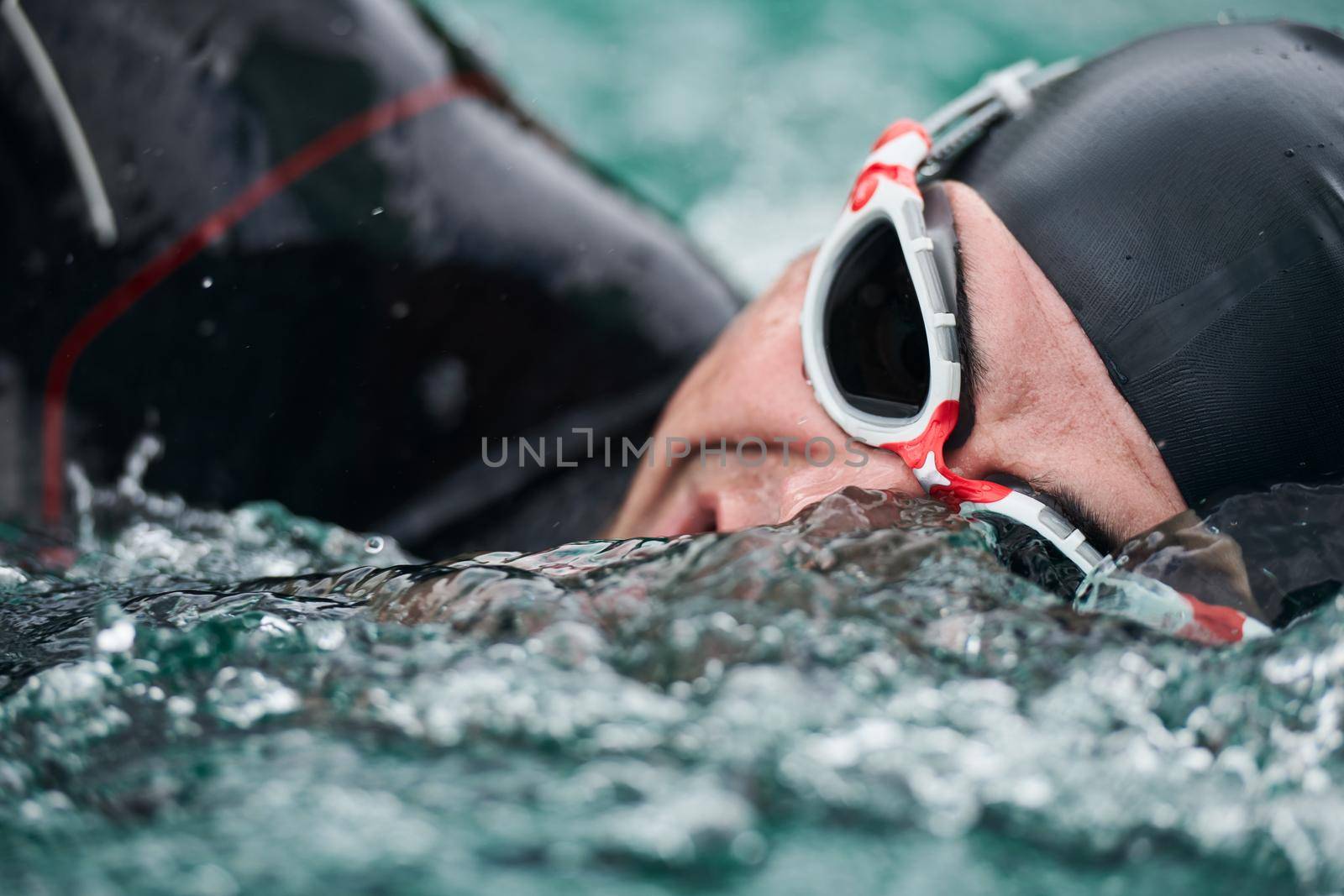 triathlon athlete swimming on lake wearing wetsuit by dotshock