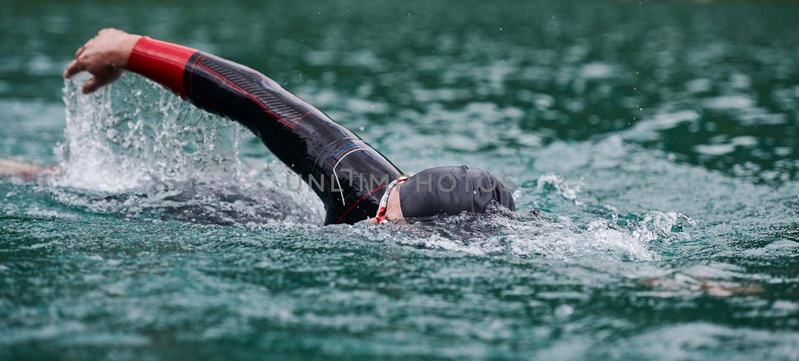 triathlon athlete swimming on extreme morning training in green lake wearing wetsuit