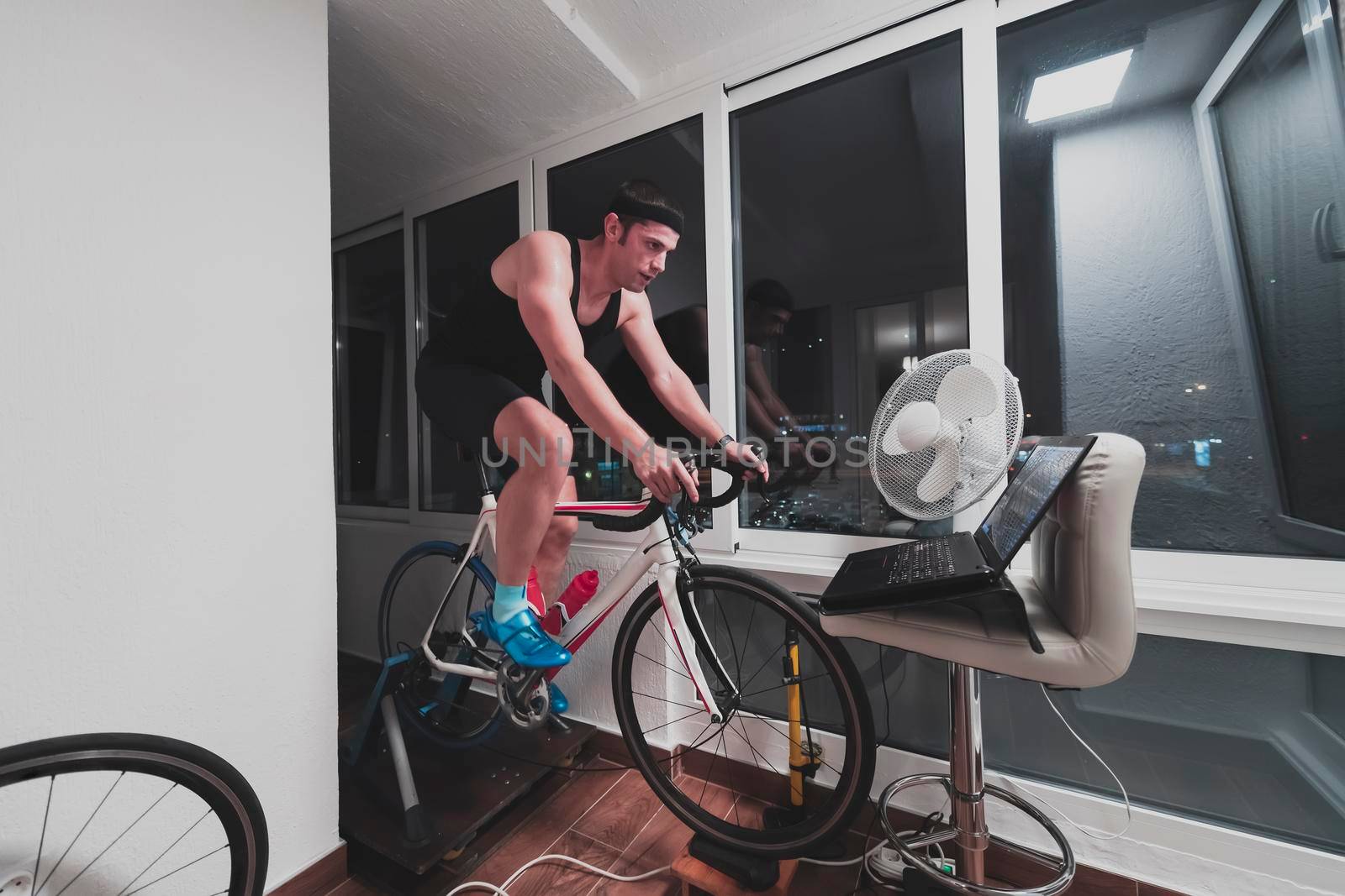 Man cycling on the machine trainer he is exercising in the home at night. Playing online bike racing game during coronavirus covid19 lockdown. New normal concept.