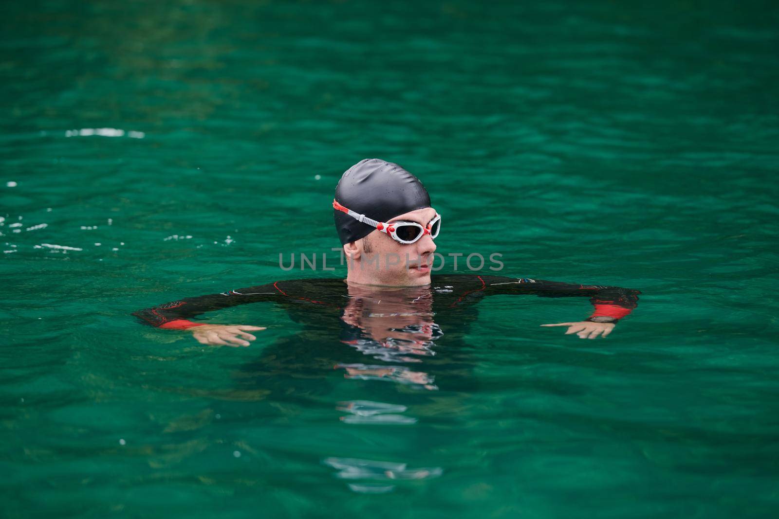 triathlon athlete swimming on extreme morning training in green lake wearing wetsuit