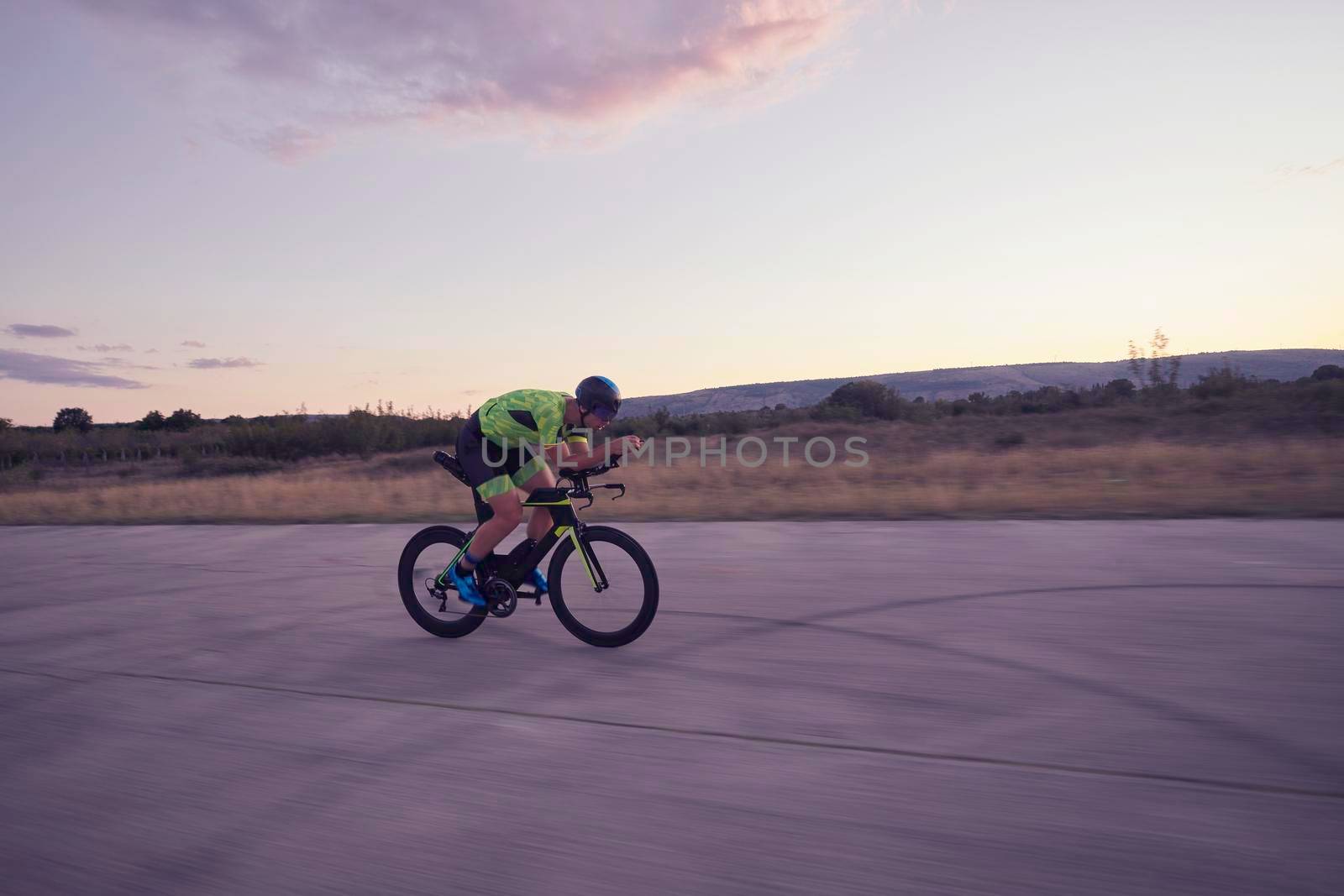 triathlon athlete riding professional racing bike on morning workout sunset or sunrise in background