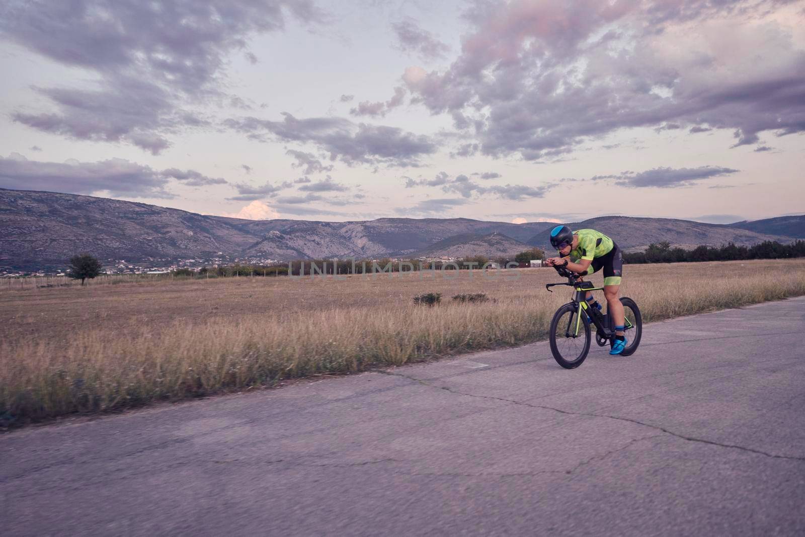 triathlon athlete riding professional racing bike on morning workout sunset or sunrise in background