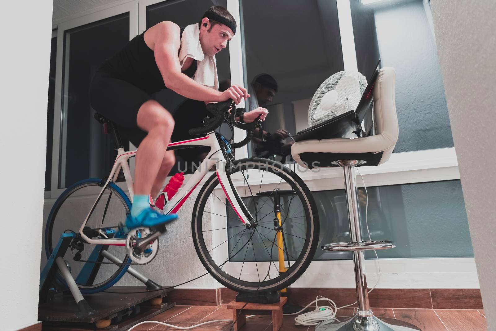 Man cycling on the machine trainer he is exercising in the home at night. Playing online bike racing game during coronavirus covid19 lockdown. New normal concept.