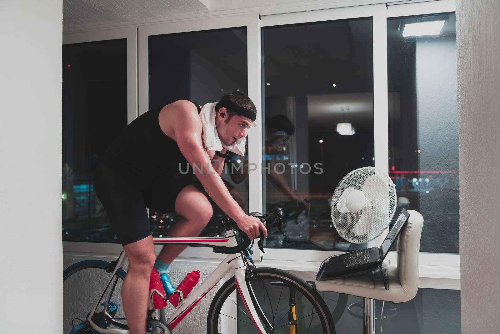 Man cycling on the machine trainer he is exercising in the home at night playing online bike racing game by dotshock