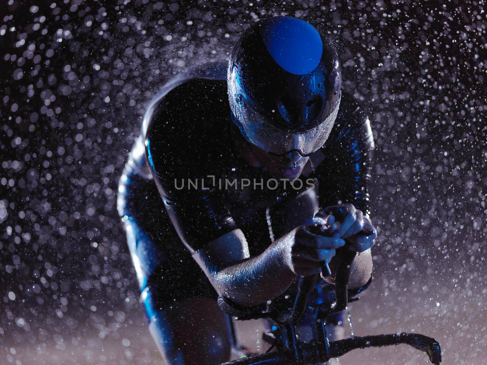 triathlon athlete riding bike on rainy night by dotshock