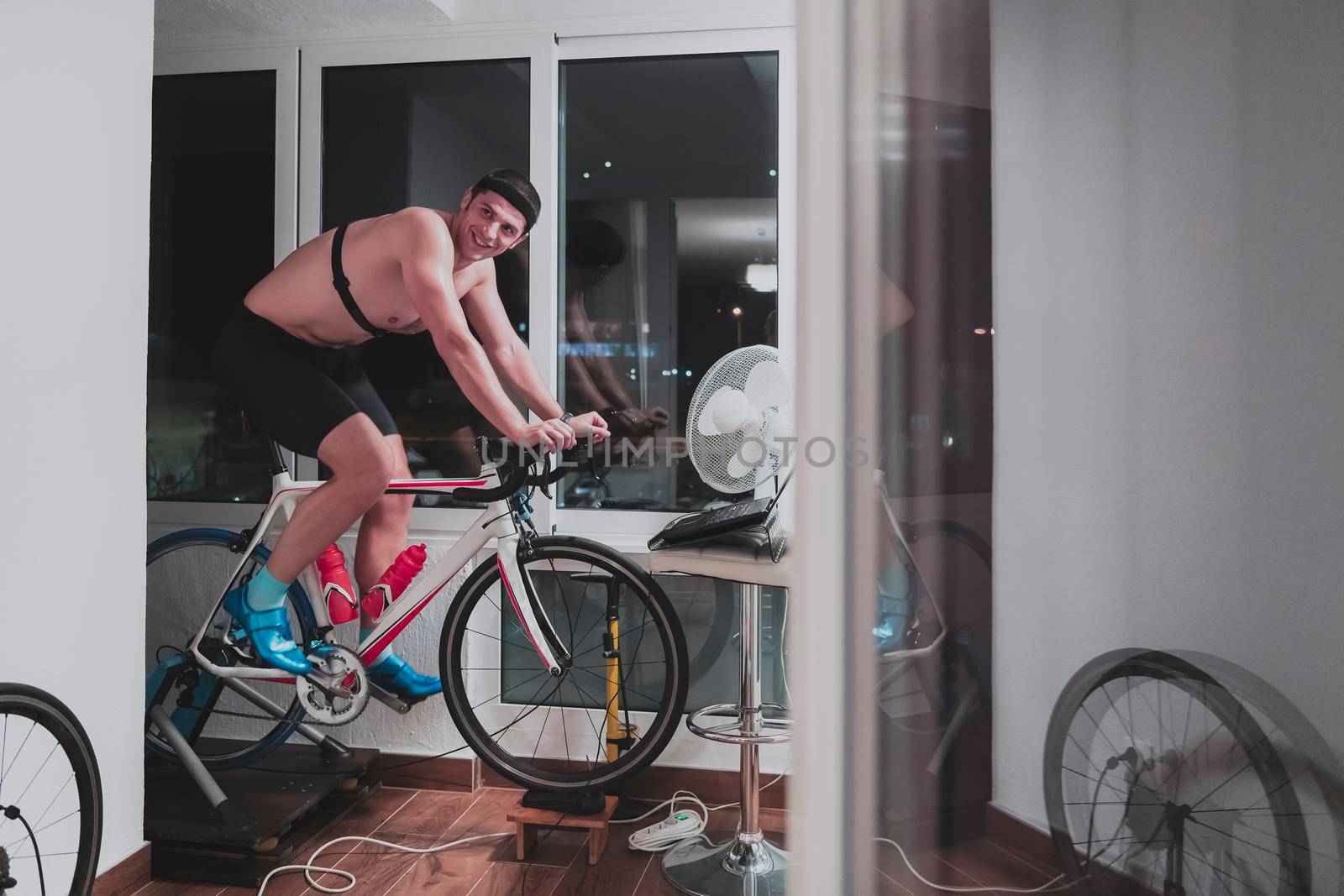 Man cycling on the machine trainer he is exercising in the home at night playing online bike racing game by dotshock