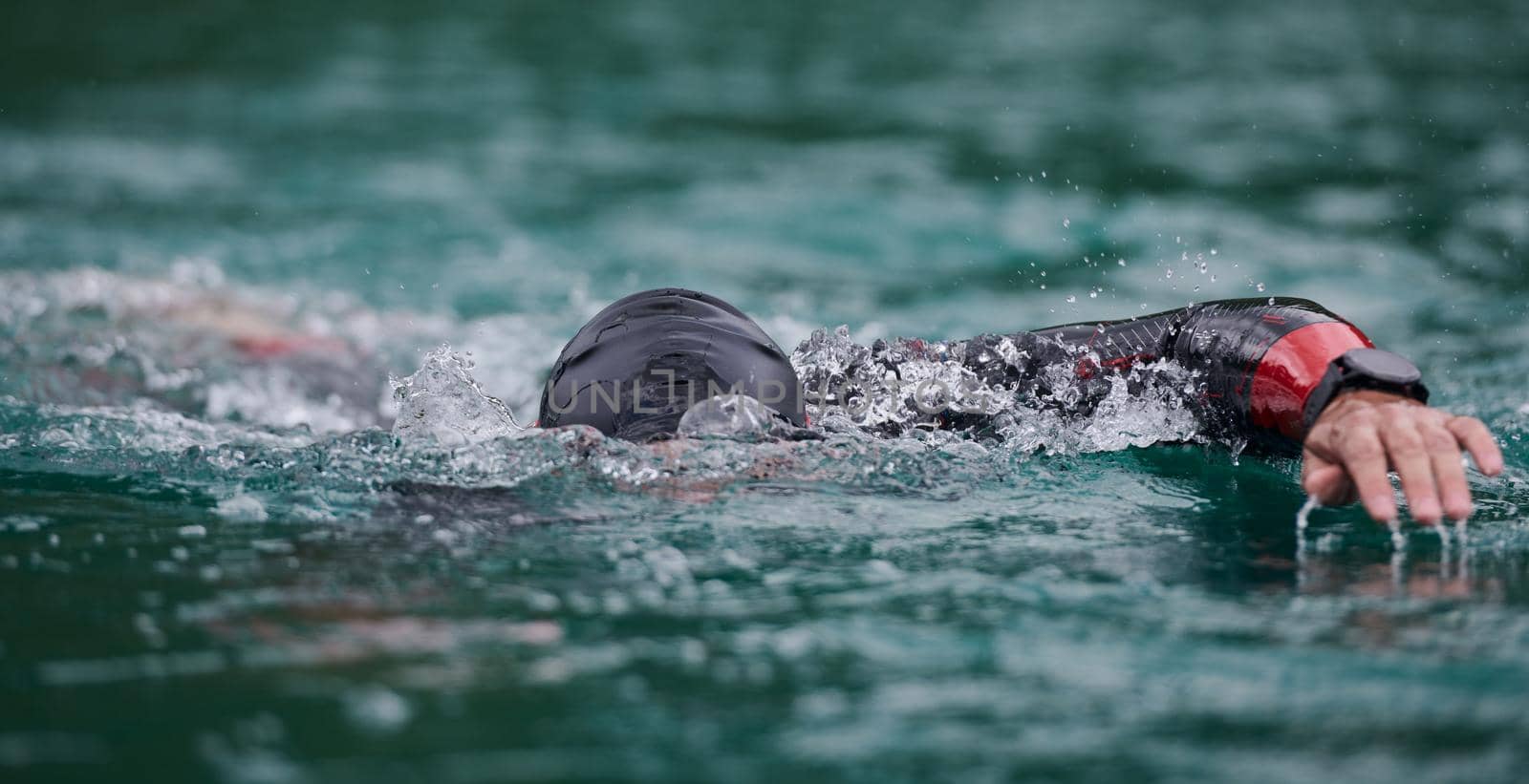 triathlon athlete swimming on lake wearing wetsuit by dotshock