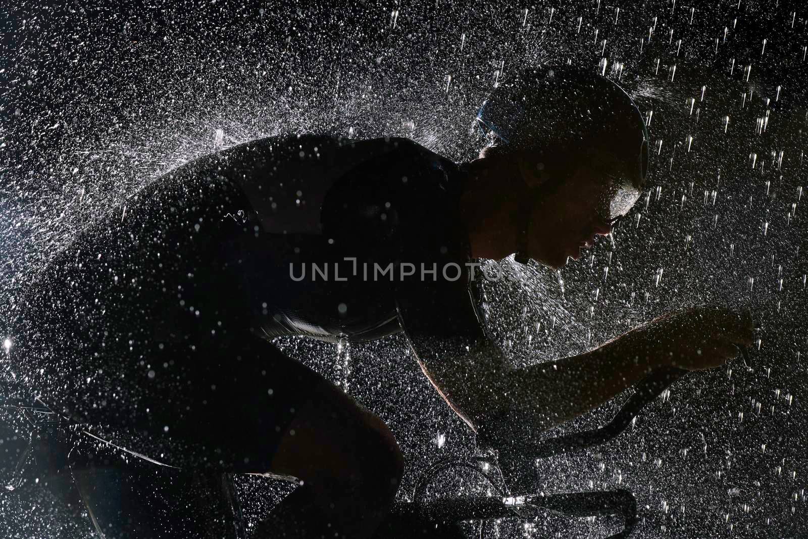 triathlon athlete riding professional racing bike fast  at night with bad weather and falling rain