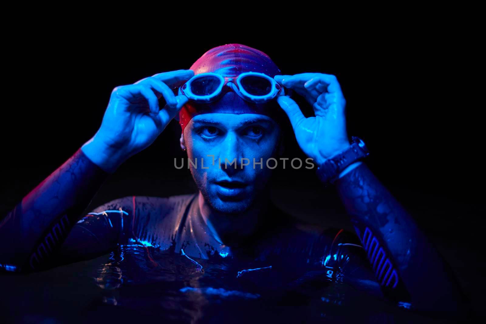 real triathlete swimmer having a break during hard training at lake on dark night neon gel color lights