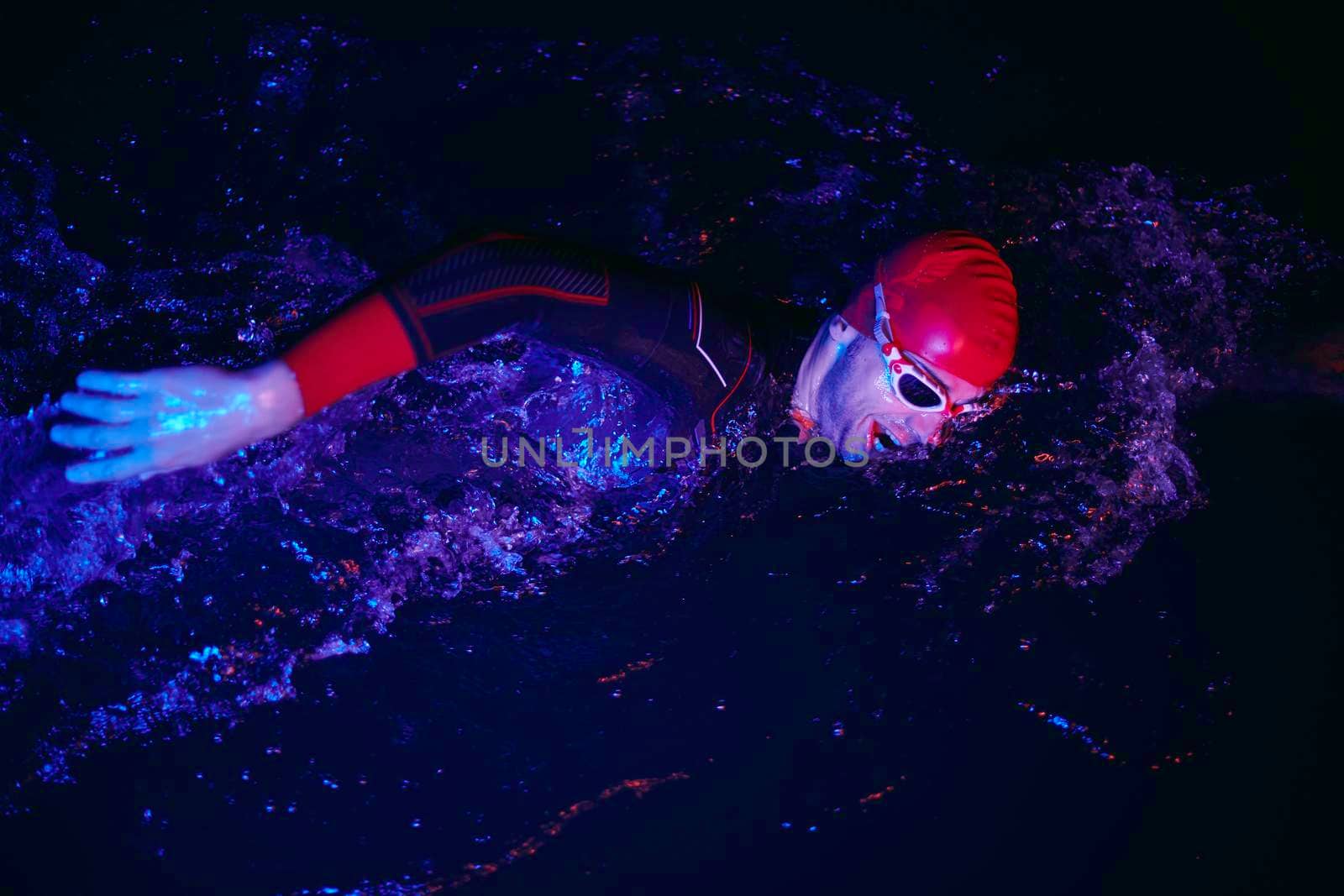 authentic triathlon swimmer have extreme training  on dark night wearing wetsuit neon gel color lights