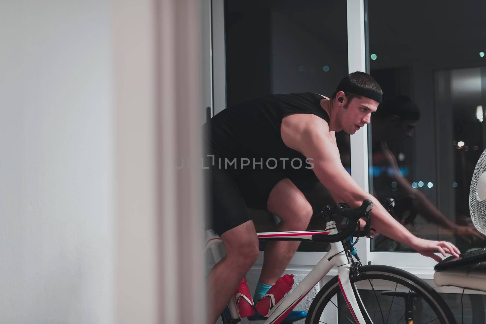 Man cycling on the machine trainer he is exercising in the home at night. Playing online bike racing game during coronavirus covid19 lockdown. New normal concept.