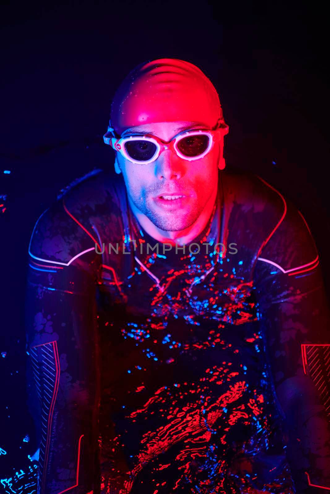 authentic triathlete swimmer having a break during hard training on night neon gel light by dotshock