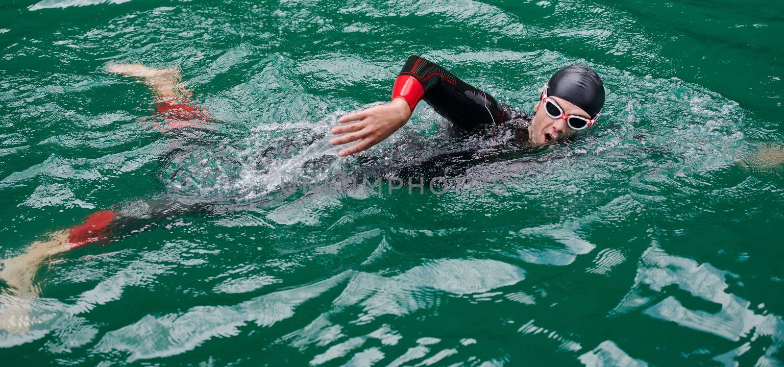 triathlon athlete swimming on lake wearing wetsuit by dotshock