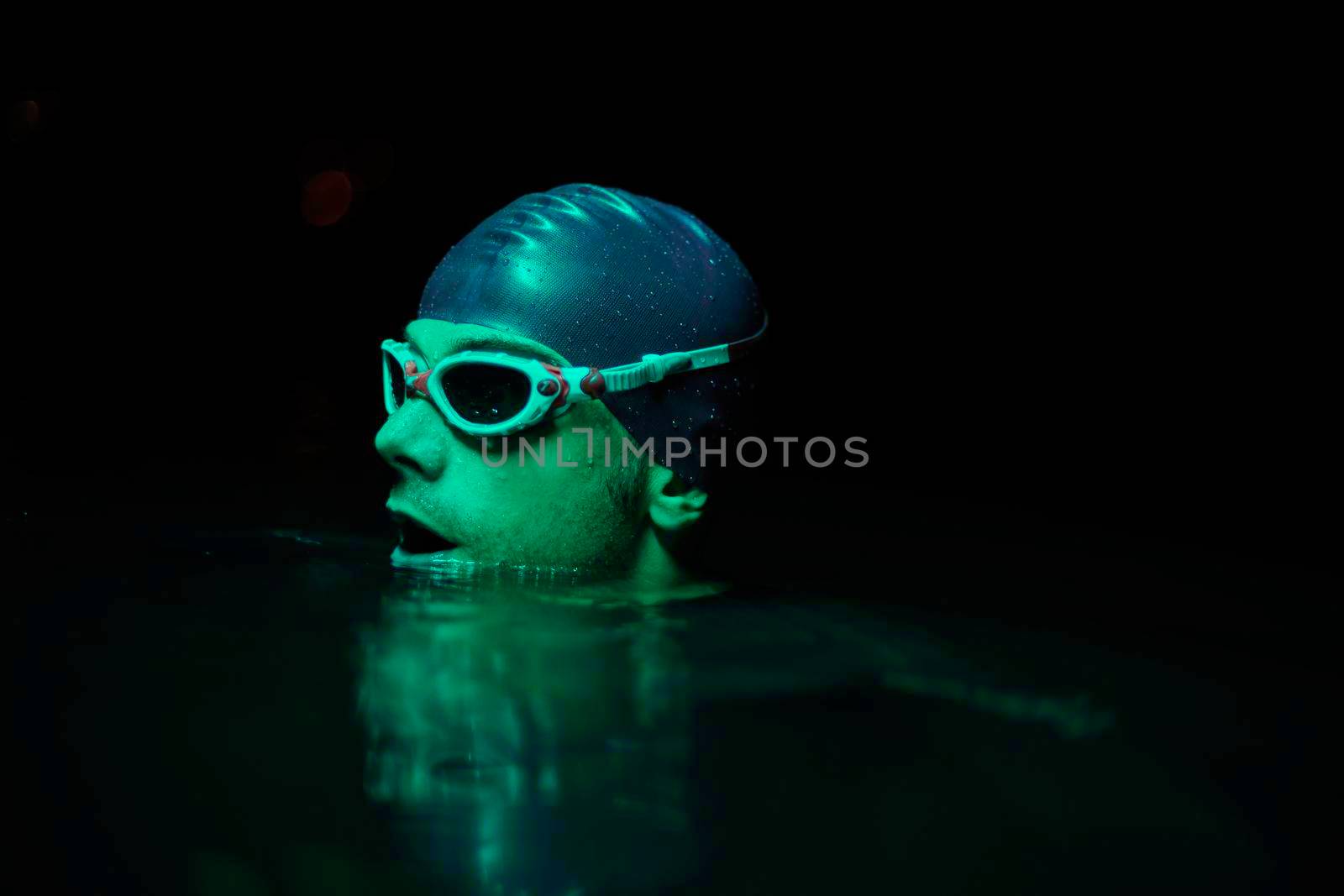 real triathlete swimmer having a break during hard training at lake on dark night neon gel color lights