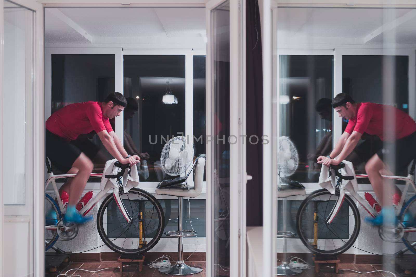 Man cycling on the machine trainer he is exercising in the home at night playing online bike racing game by dotshock