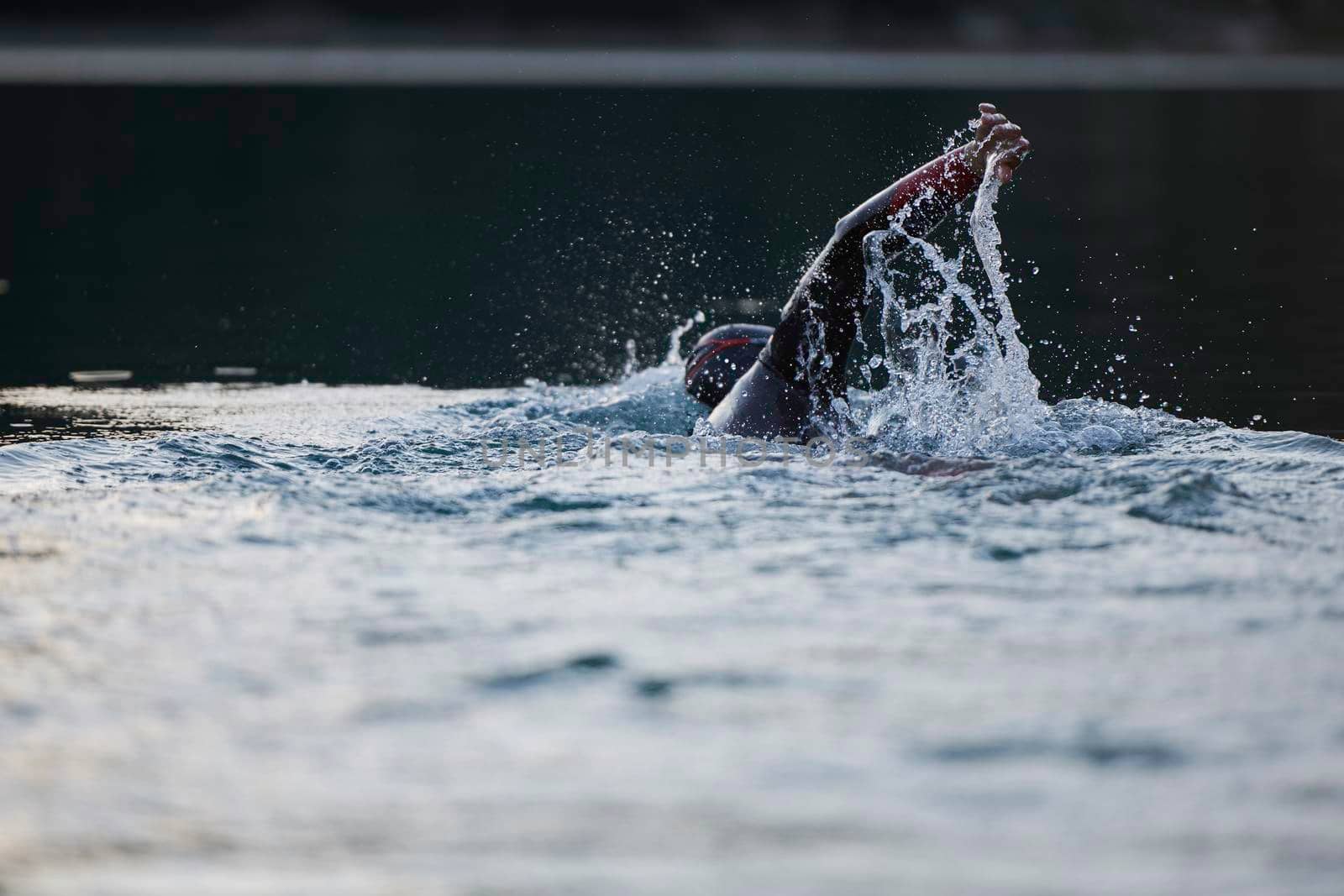 triathlon athlete swimming on beautiful morning sunrise training in lake wearing wetsuit concept of strength and endurance