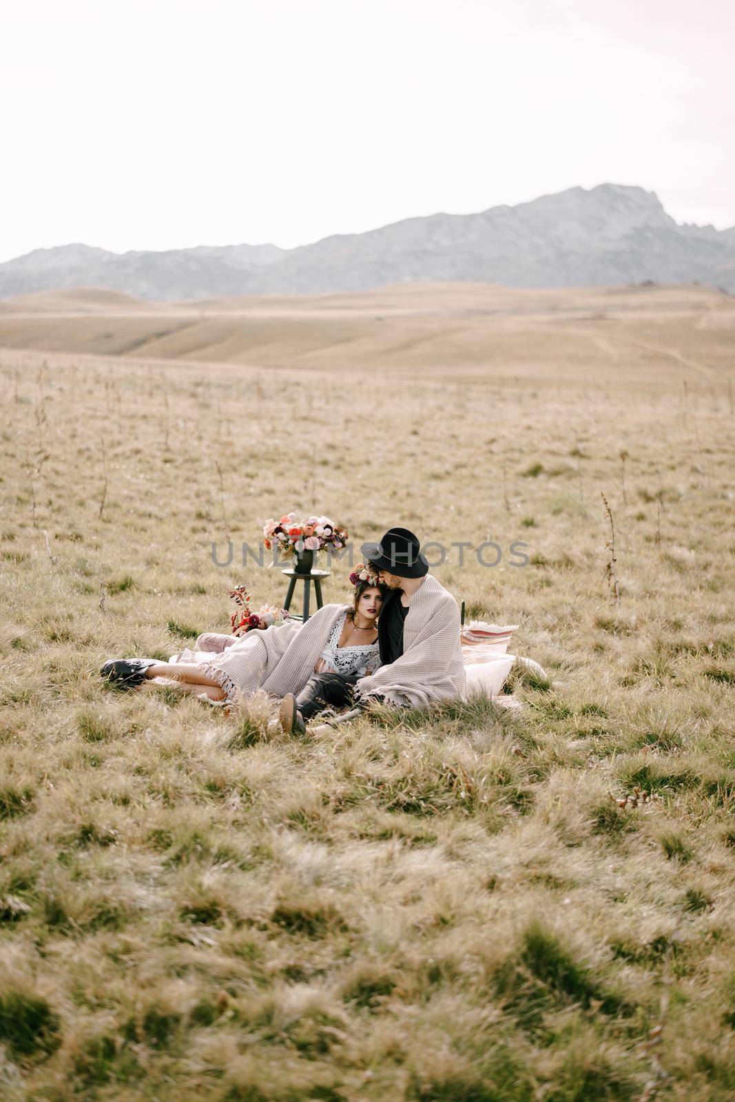 Man and woman sit on a blanket on the lawn against the backdrop of mountains. High quality photo