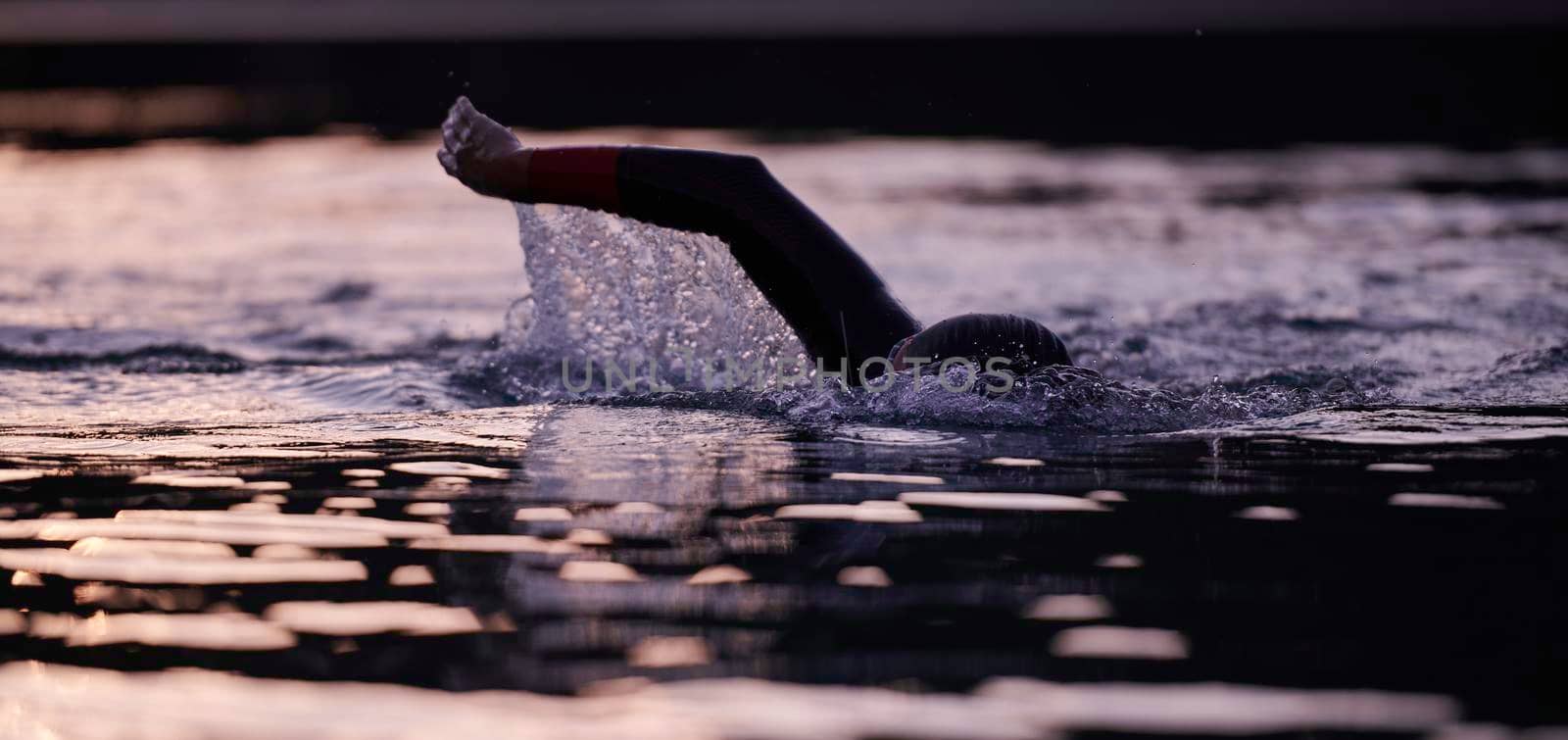 triathlon athlete swimming on beautiful morning sunrise training in lake wearing wetsuit concept of strength and endurance