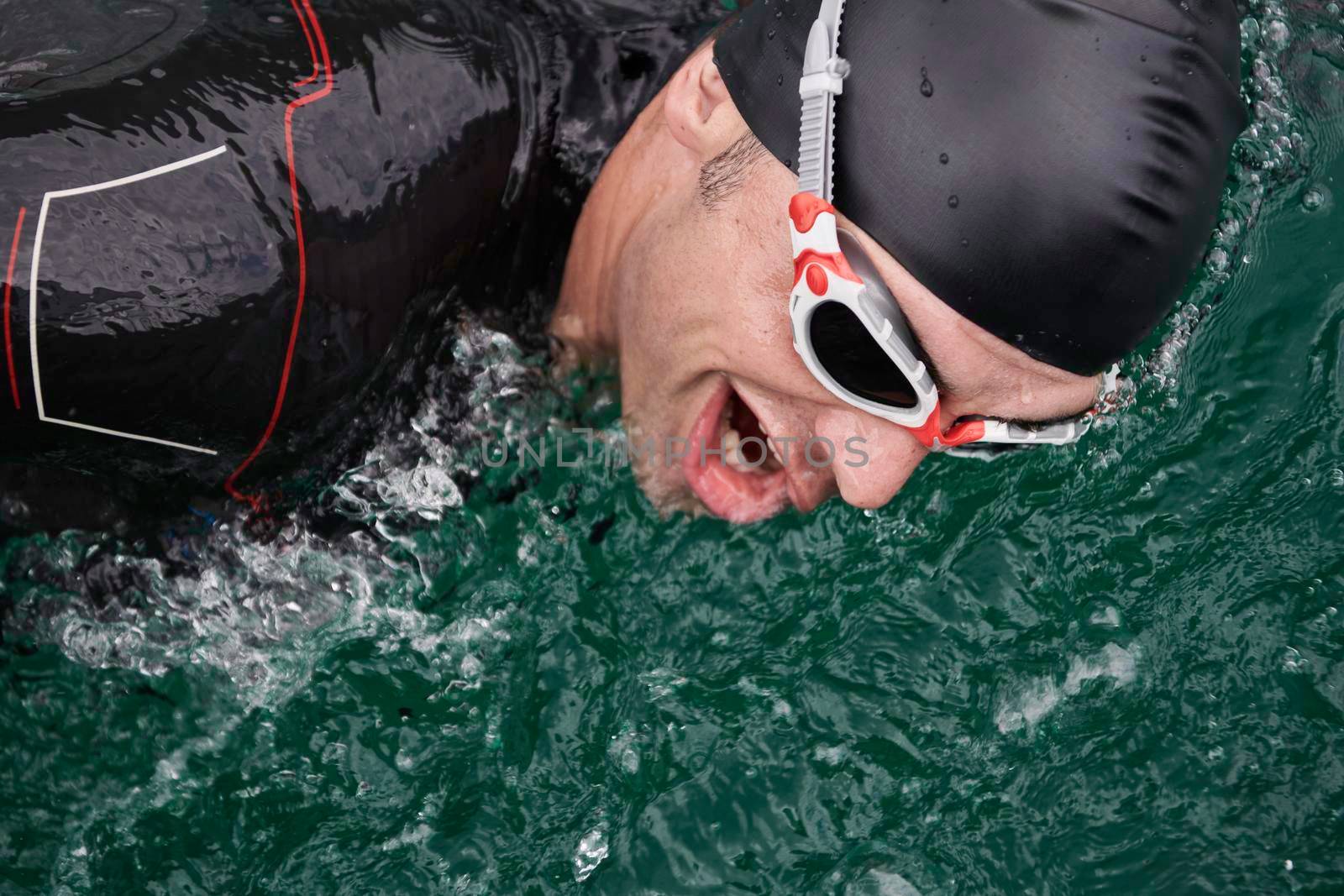 triathlon athlete swimming on extreme morning training in green lake wearing wetsuit