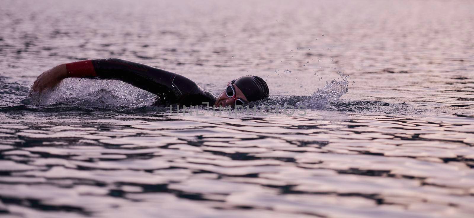 triathlon athlete swimming on beautiful morning sunrise training in lake wearing wetsuit concept of strength and endurance