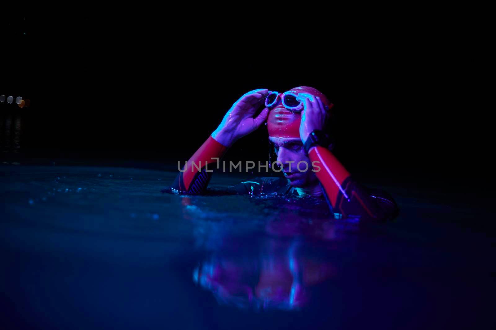 real triathlete swimmer having a break during hard training at lake on dark night neon gel color lights