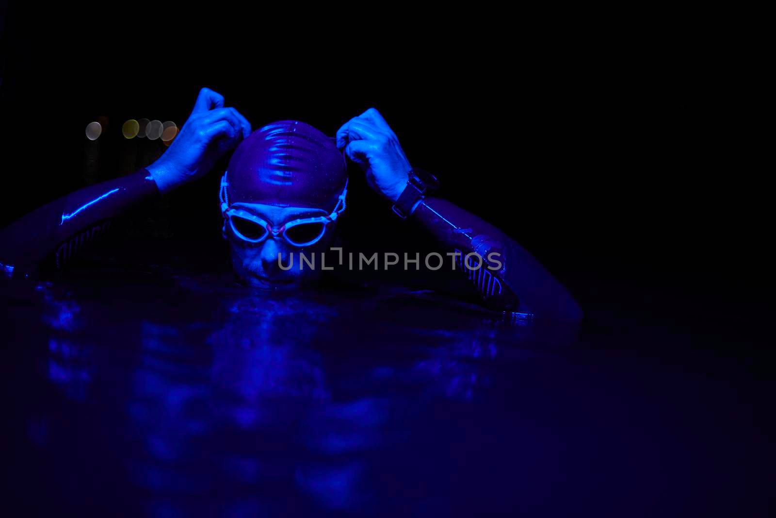 real triathlete swimmer having a break during hard training at lake on dark night neon gel color lights