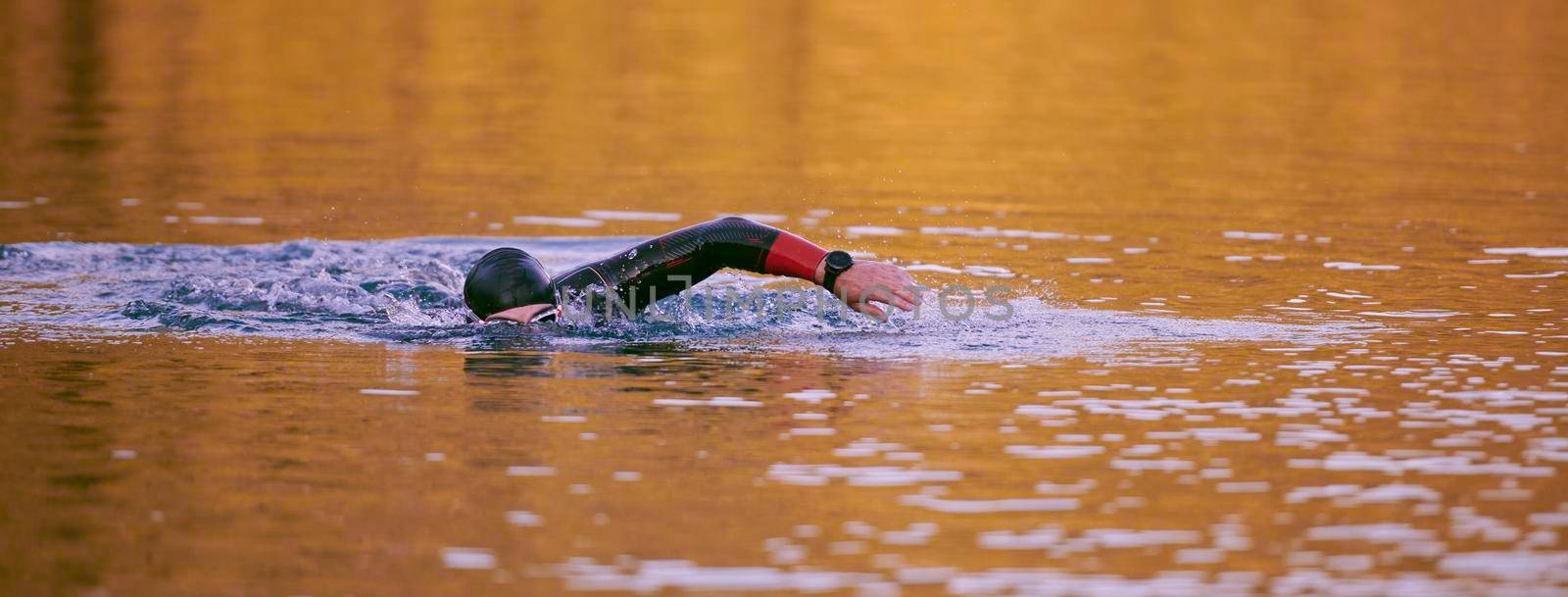 triathlon athlete swimming on beautiful morning sunrise training in lake wearing wetsuit concept of strength and endurance