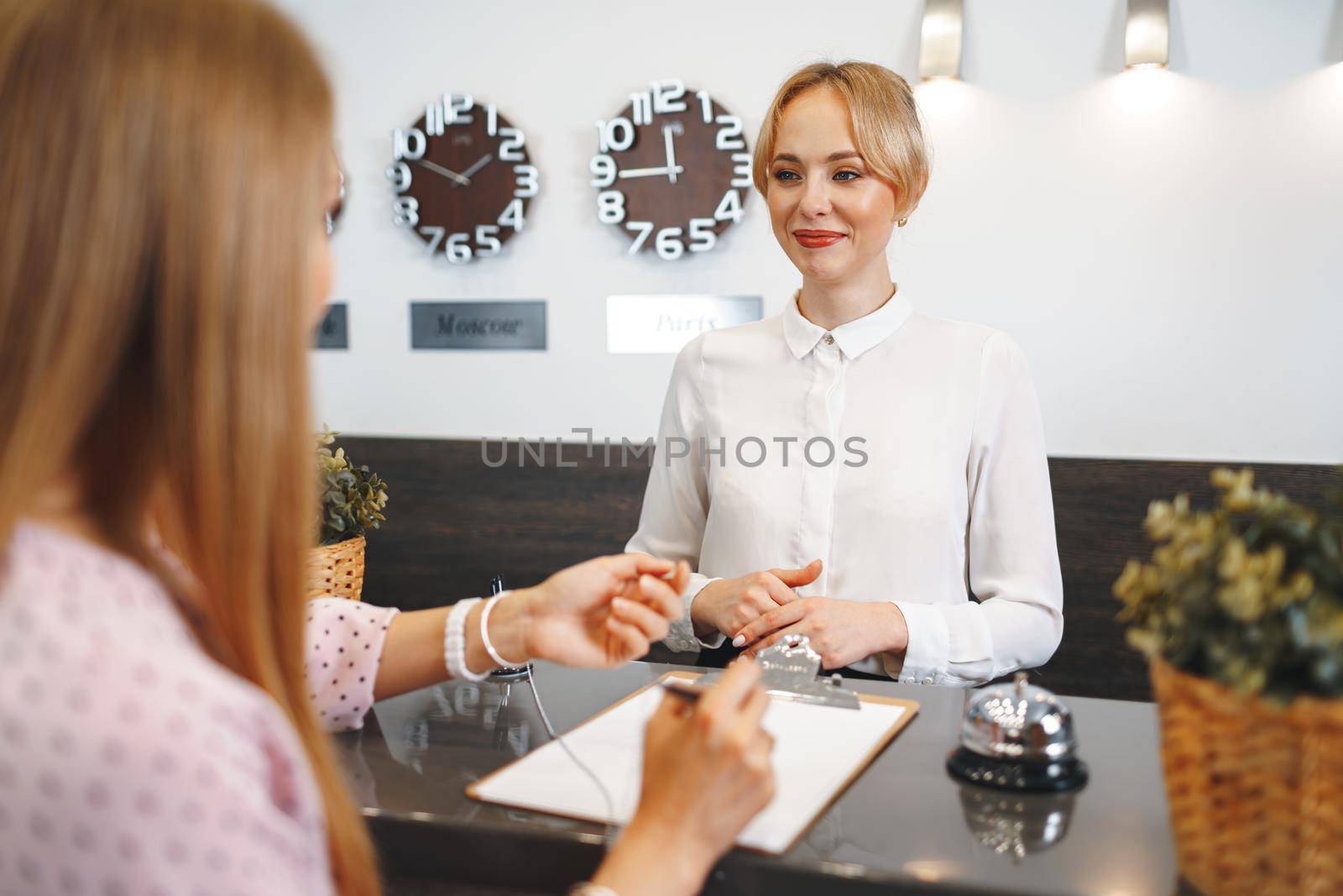 Blonde woman hotel guest checking-in at front desk in hotel close up