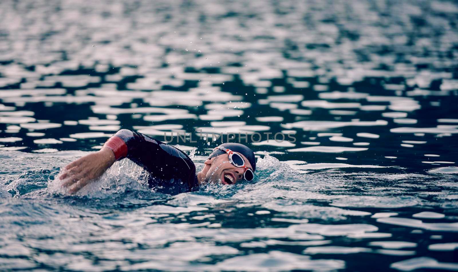 triathlon athlete swimming on beautiful morning sunrise training in lake wearing wetsuit concept of strength and endurance