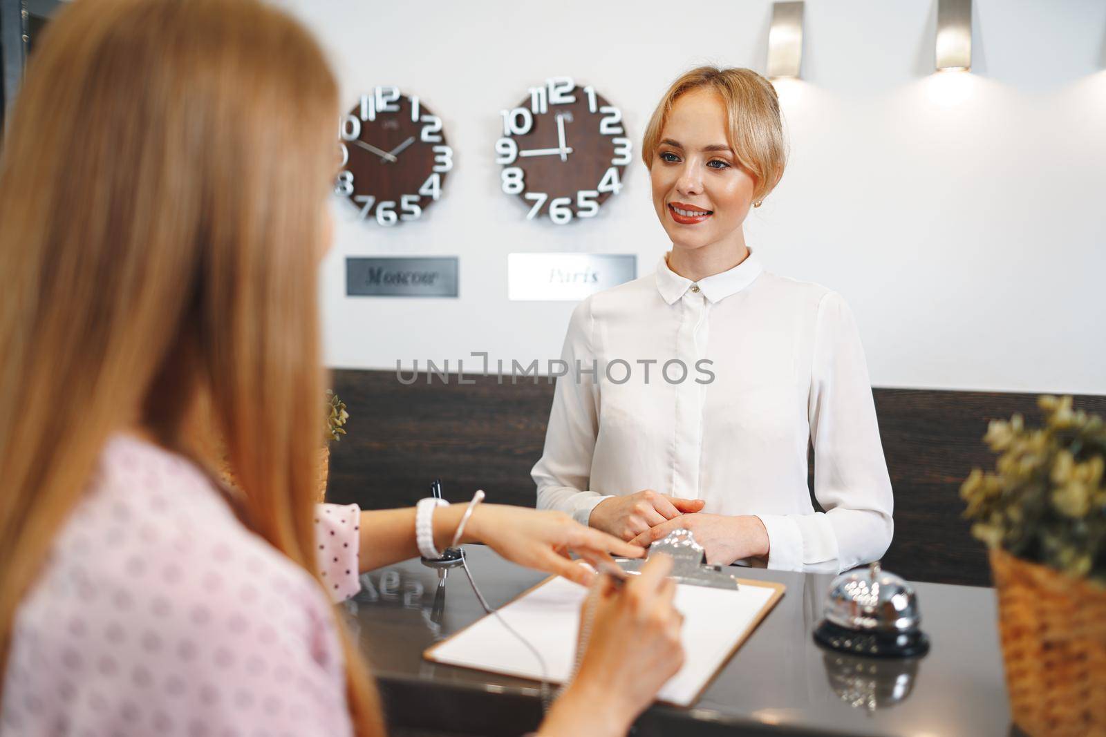 Blonde woman hotel guest checking-in at front desk in hotel close up