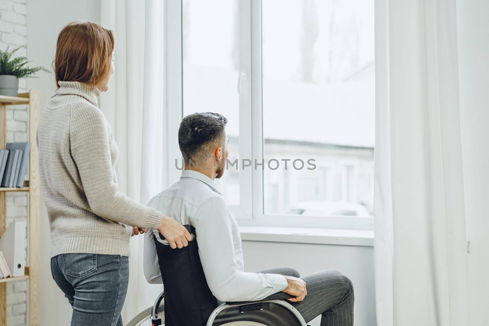 Woman caring for disabled man in wheelchair at home close up