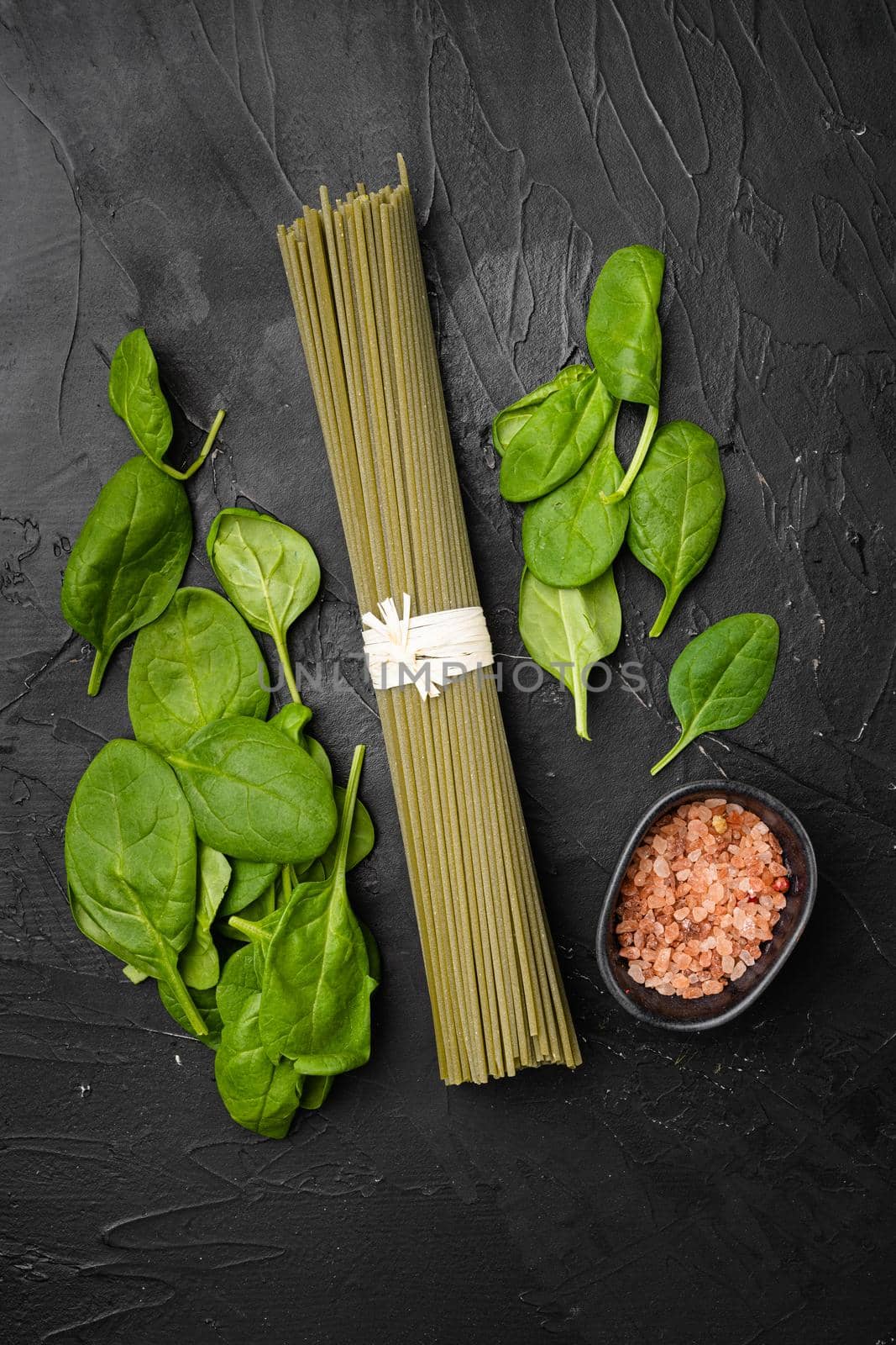 Green colored spaghetti raw dry spinach set, on black dark stone table background, top view flat lay