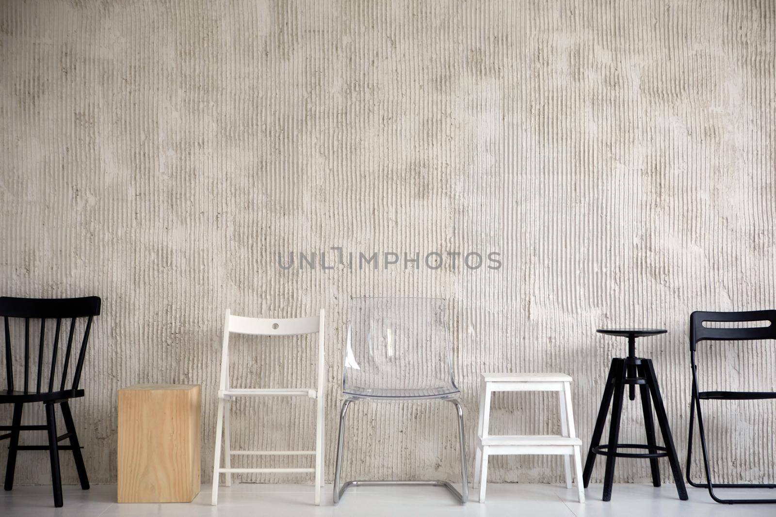 Wooden plastic and metal chairs placed in row near cement wall in studio. Different types configurations and materials of chair