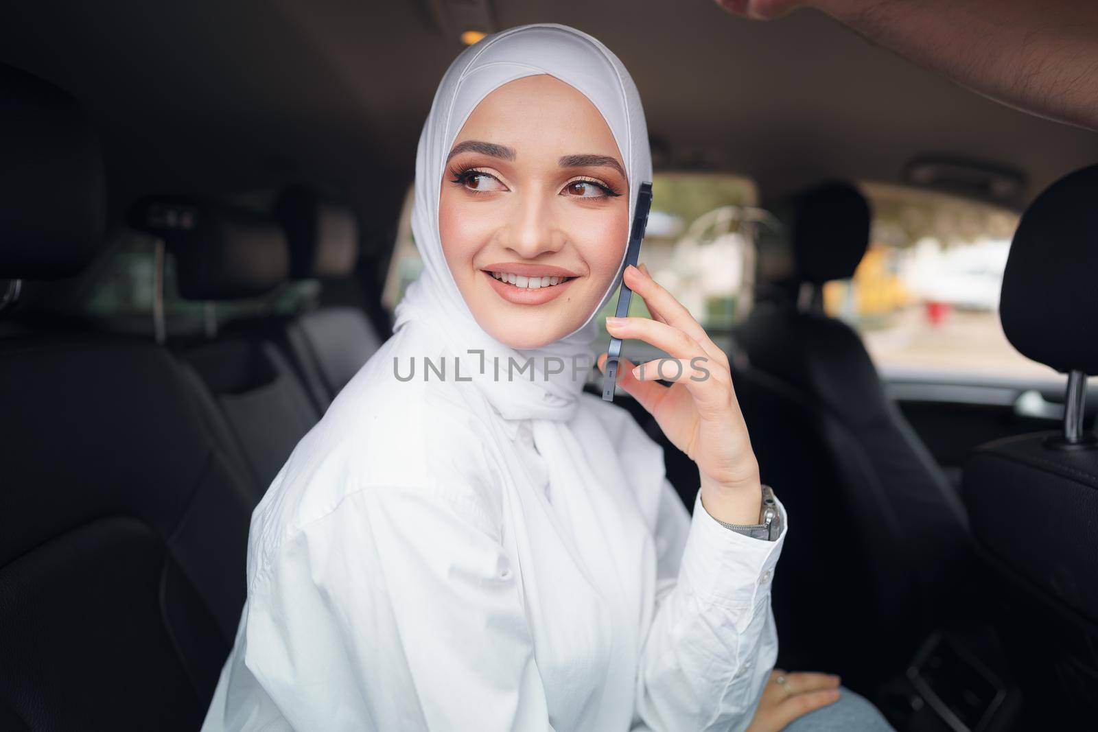 Beautiful young woman in hijab sitting in a car and talking on the phone, close up