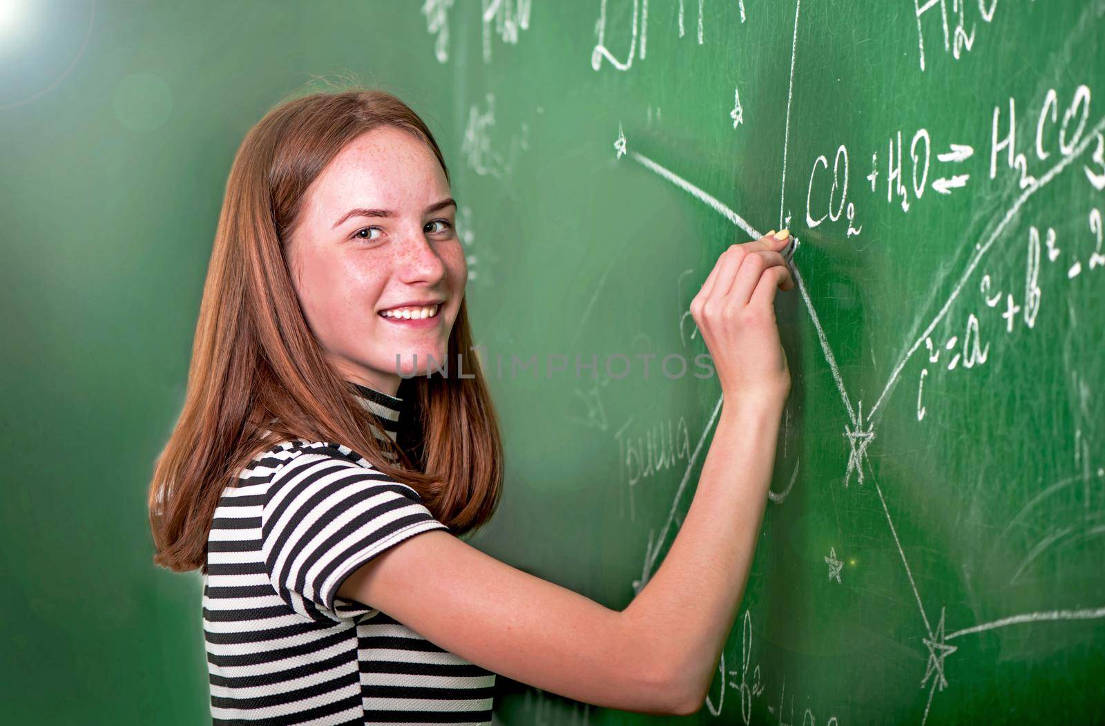 Student girl standing near clean blackboard in the classroom.