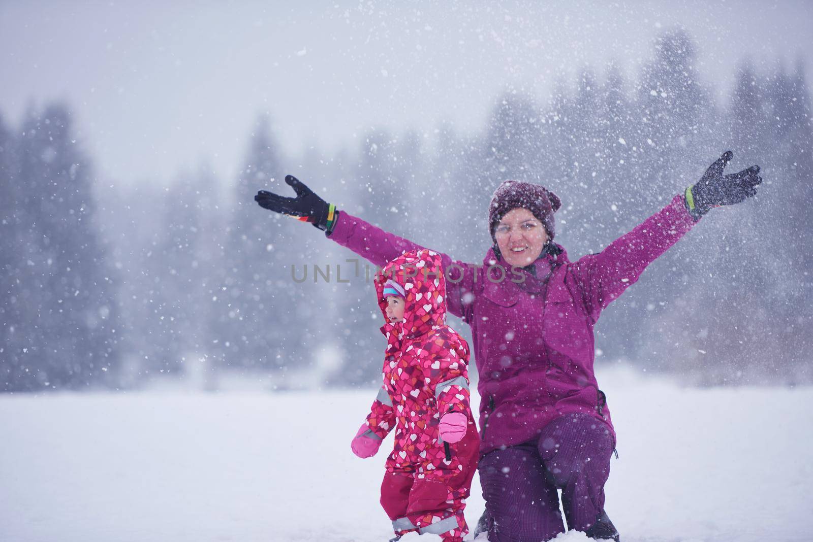 happy family on winter vacation, mom and cute little girl have fun and slide while snow falkes falling