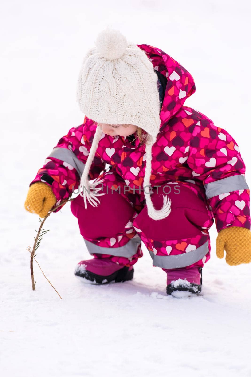 happy cute little girl wearing a red snow suit and white hat  while having fun and playing on fresh snow at snowy winter day