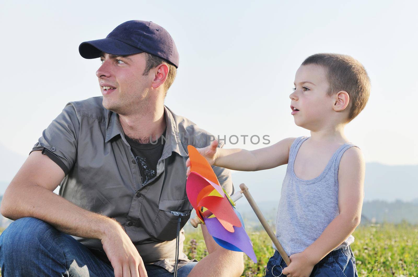 little happy child and young father  play with windmil toy and have  fun while running on beautiful meadow at sunset 