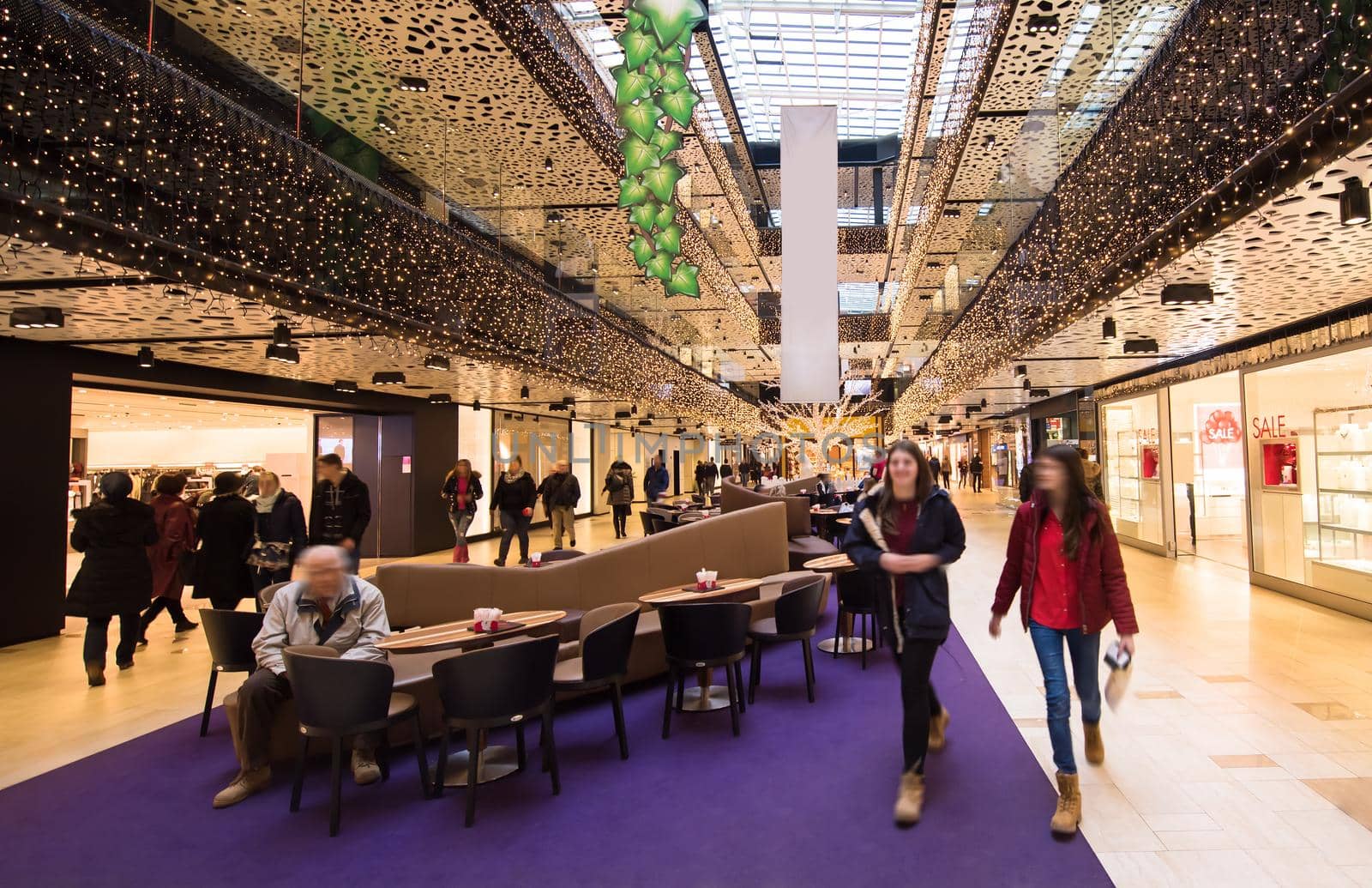 Shoppers walking through luxury shopping mall interior  Interior of big modern shopping mall with some people in it