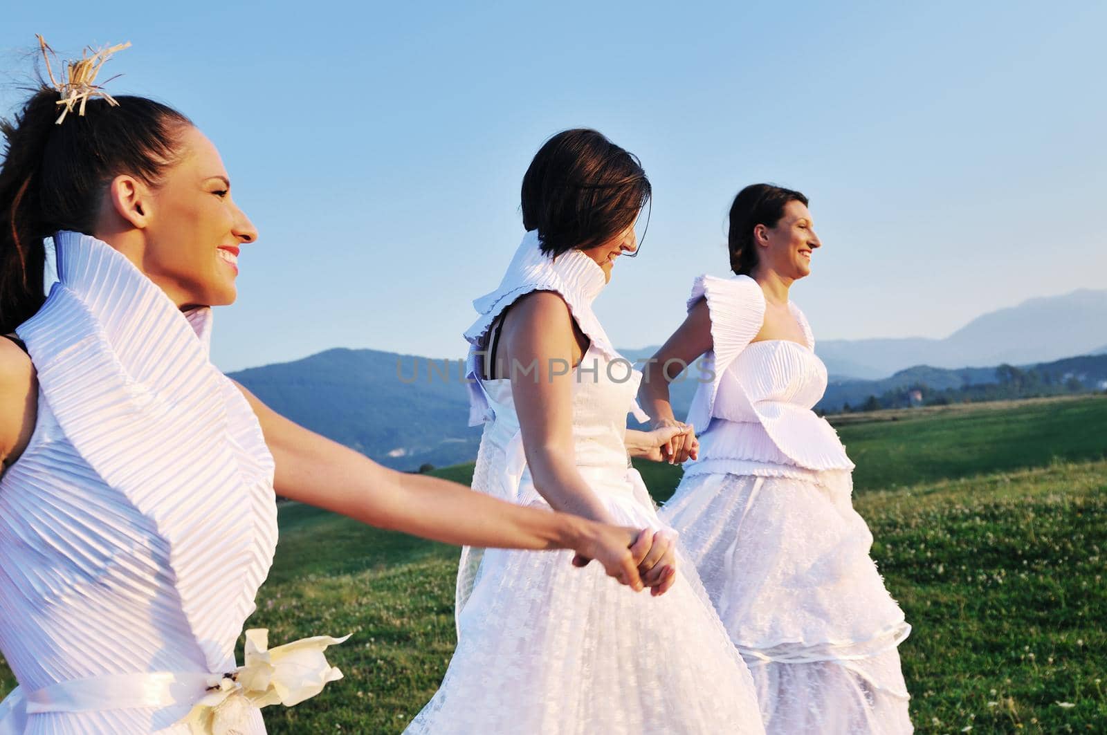 group of bride run on meadow at sunset after wedding party