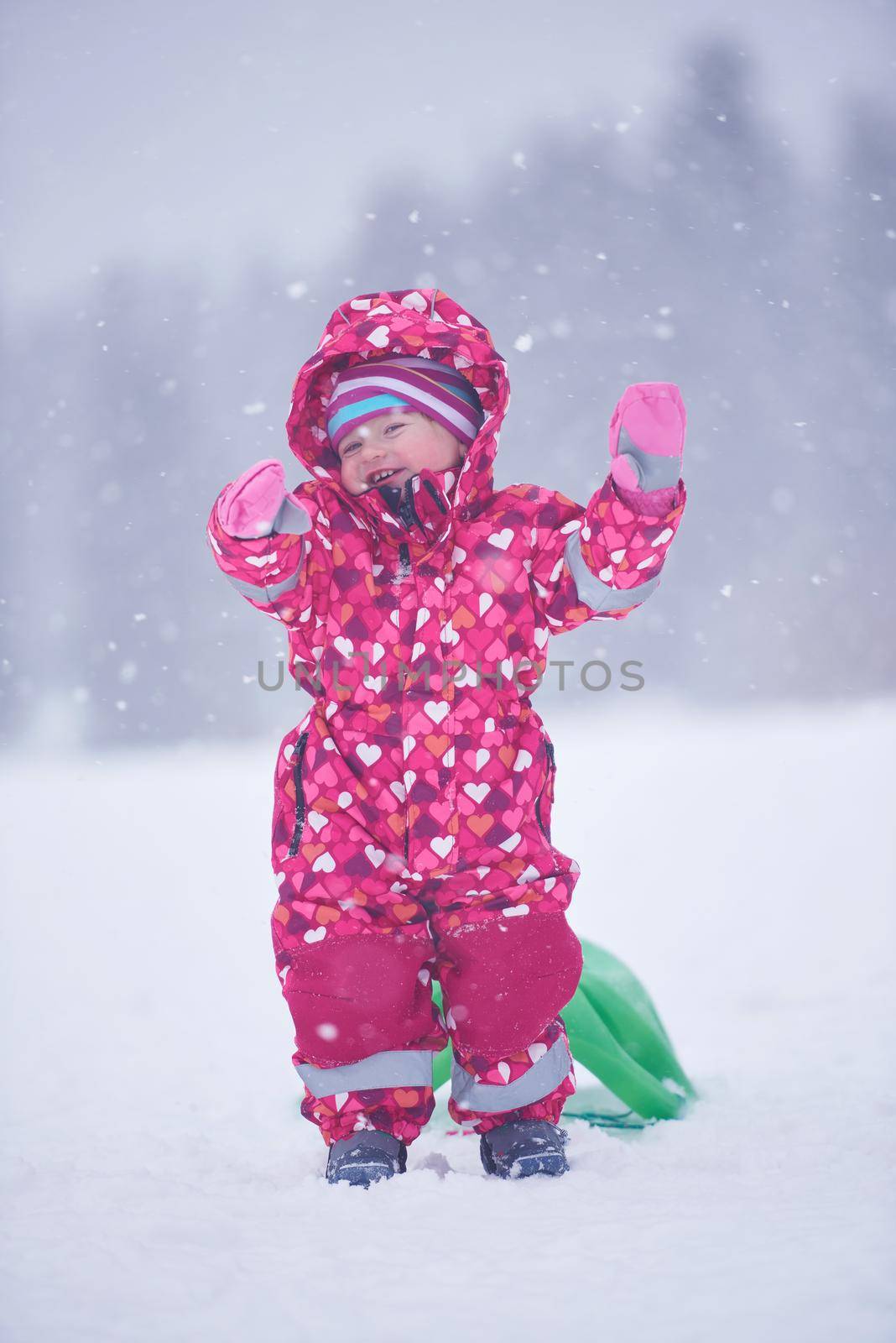 happy family on winter vacation, mom and cute little girl have fun and slide while snow falkes falling