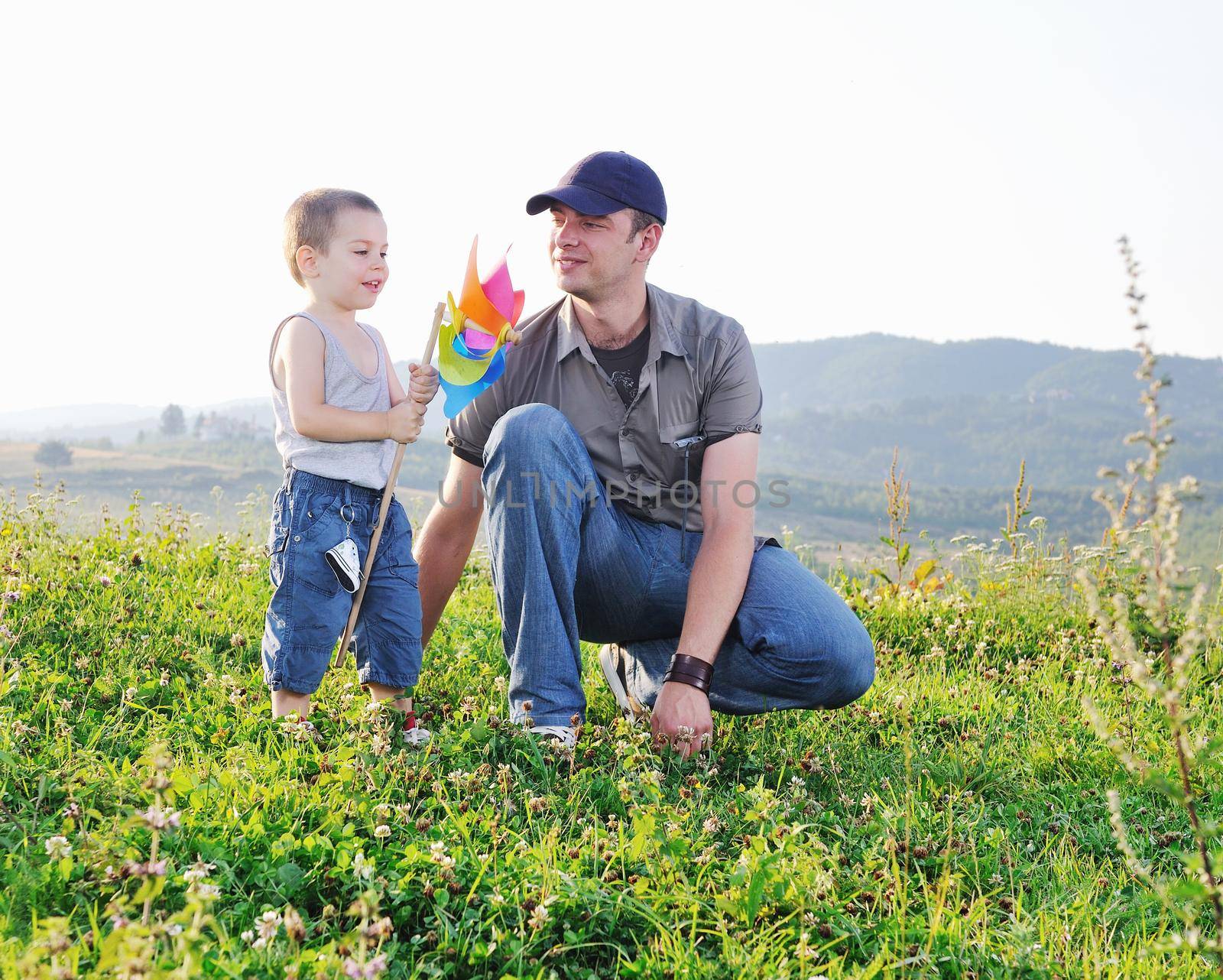 little happy child and young father  play with windmil toy and have  fun while running on beautiful meadow at sunset 