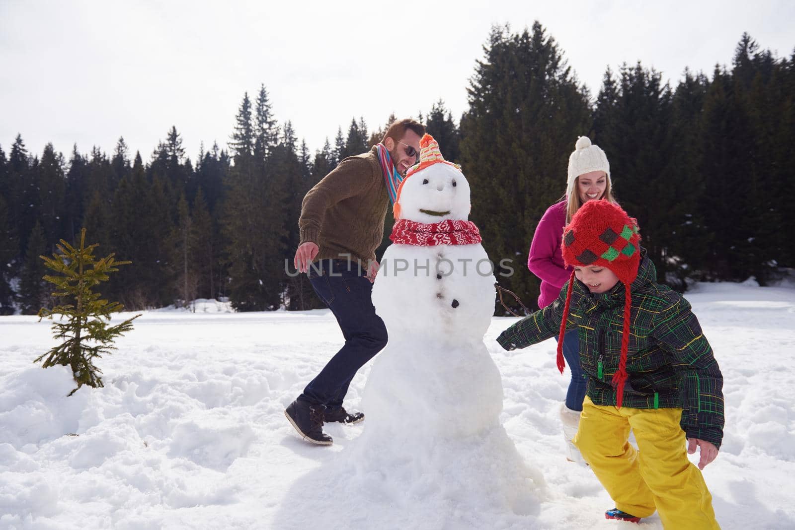 happy young  family playing in fresh snow and building snowman at beautiful sunny winter day outdoor in nature