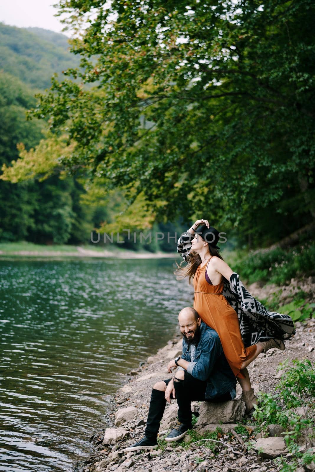Pregnant woman leaning against a sitting laughing man on the lake. High quality photo