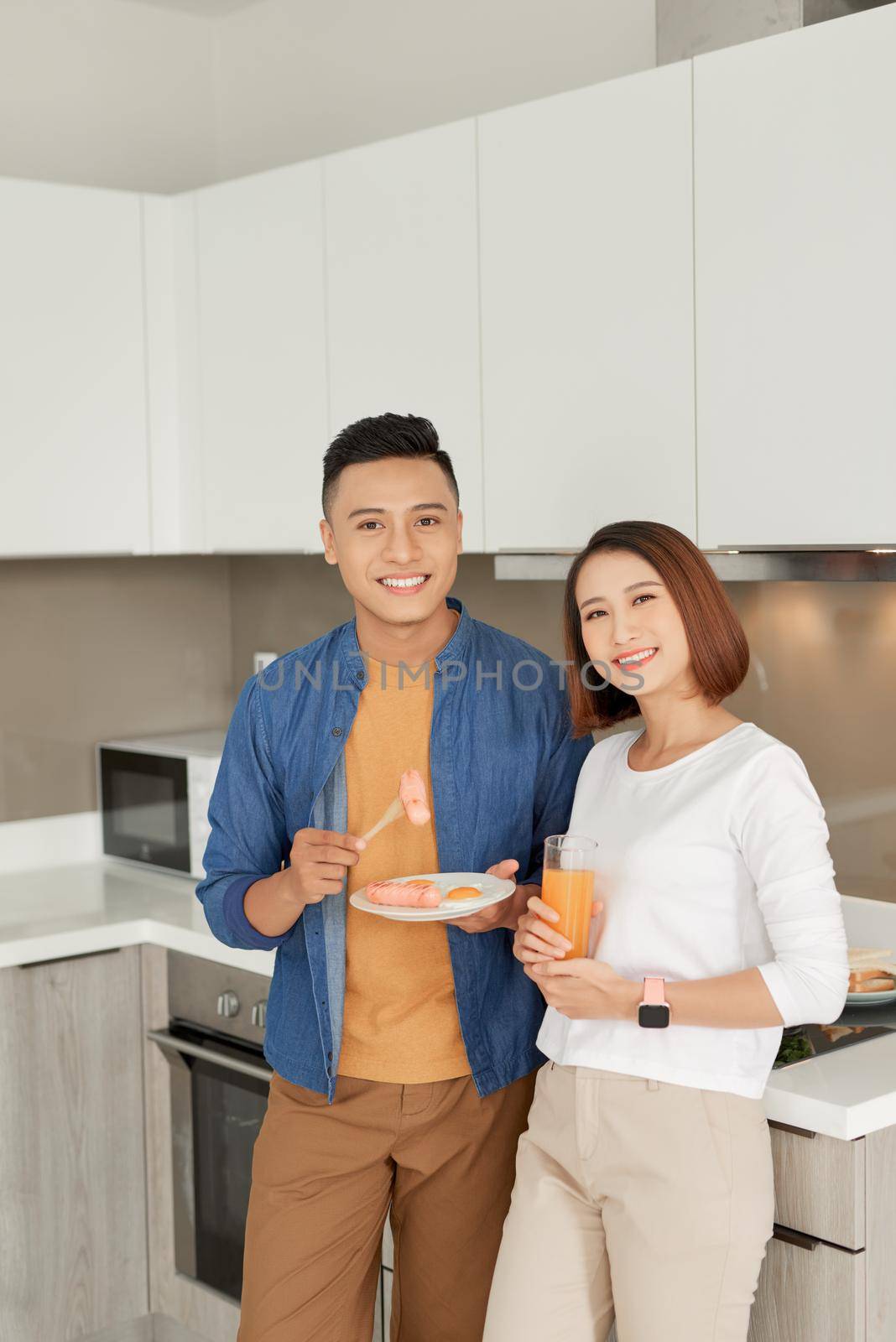 Beautiful young couple is feeding each other and smiling while cooking in kitchen at home