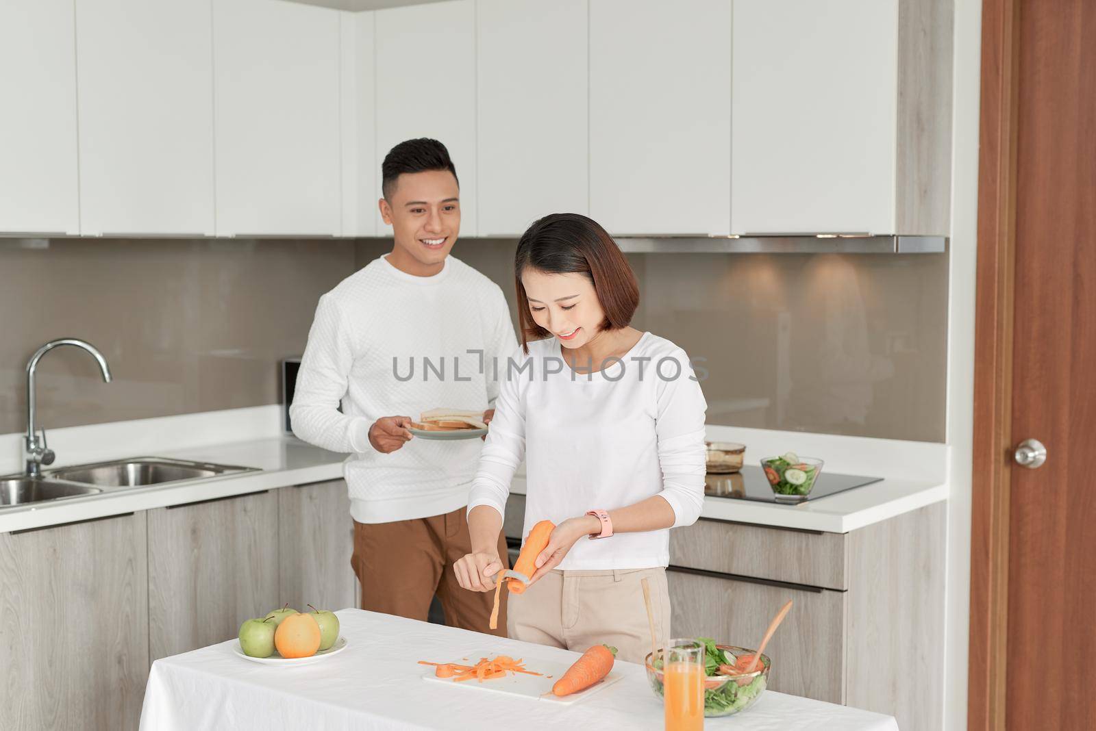 Beautiful young couple is feeding each other and smiling while cooking in kitchen at home