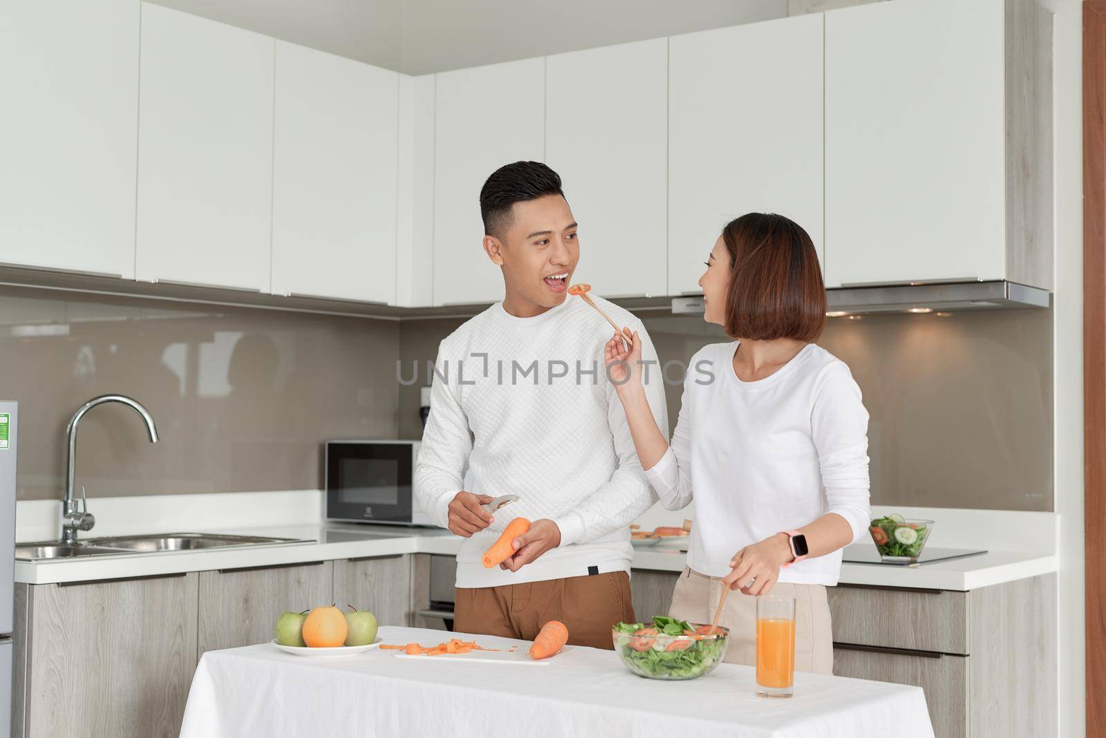 Happy couple standing in kitchen at home preparing together yummy dinner on first dating by makidotvn