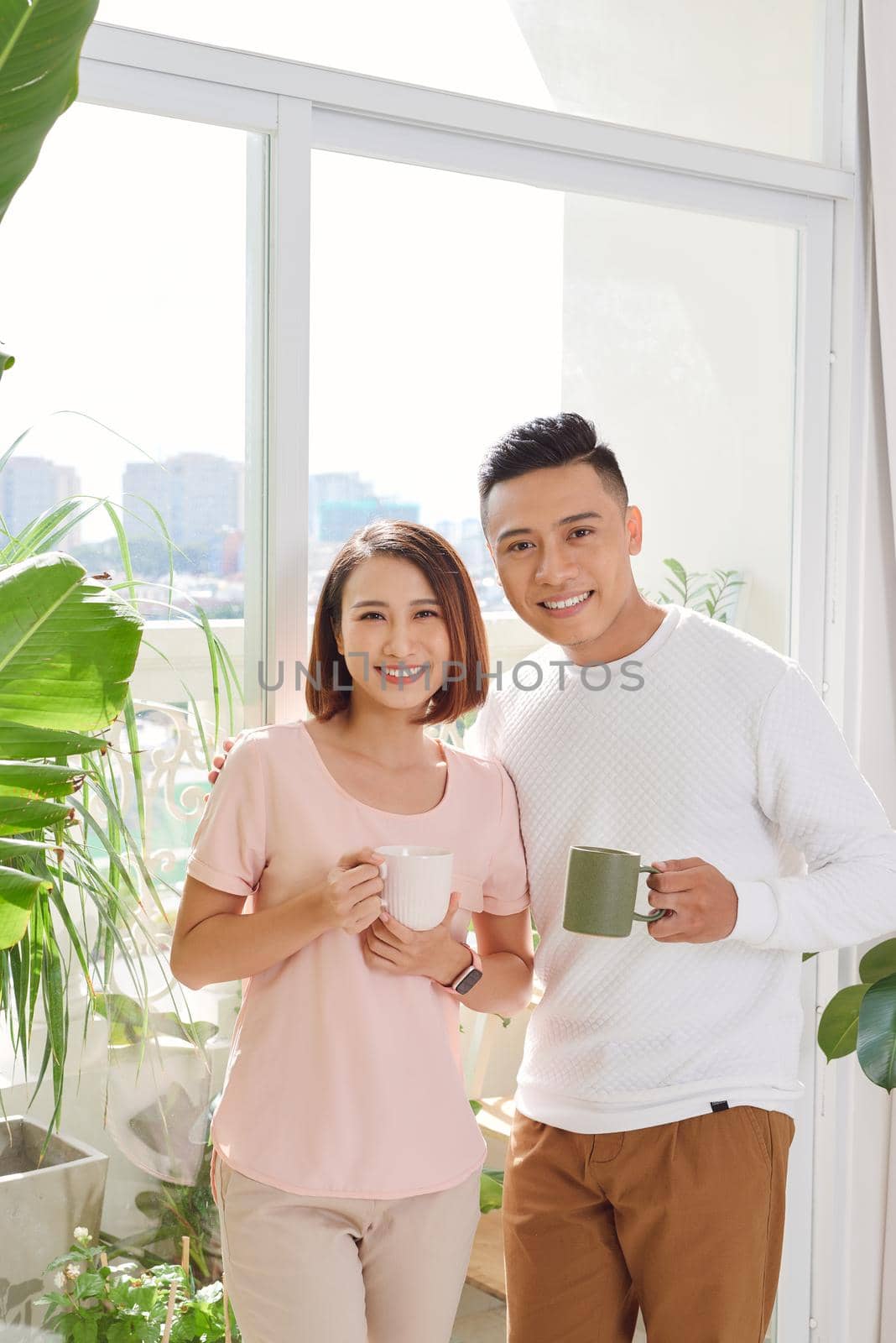  cute smiling young Asian lover couple standing near the windows in the living room in morning by makidotvn