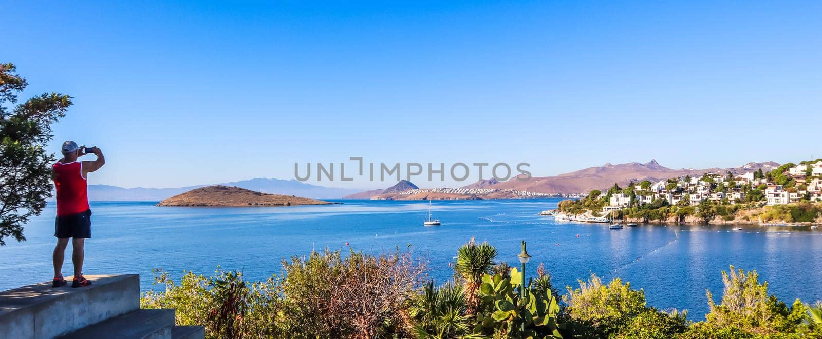 A tourist photographs a lovely view of beautiful bay with calm blue water. Rest and relaxation on the sea coast