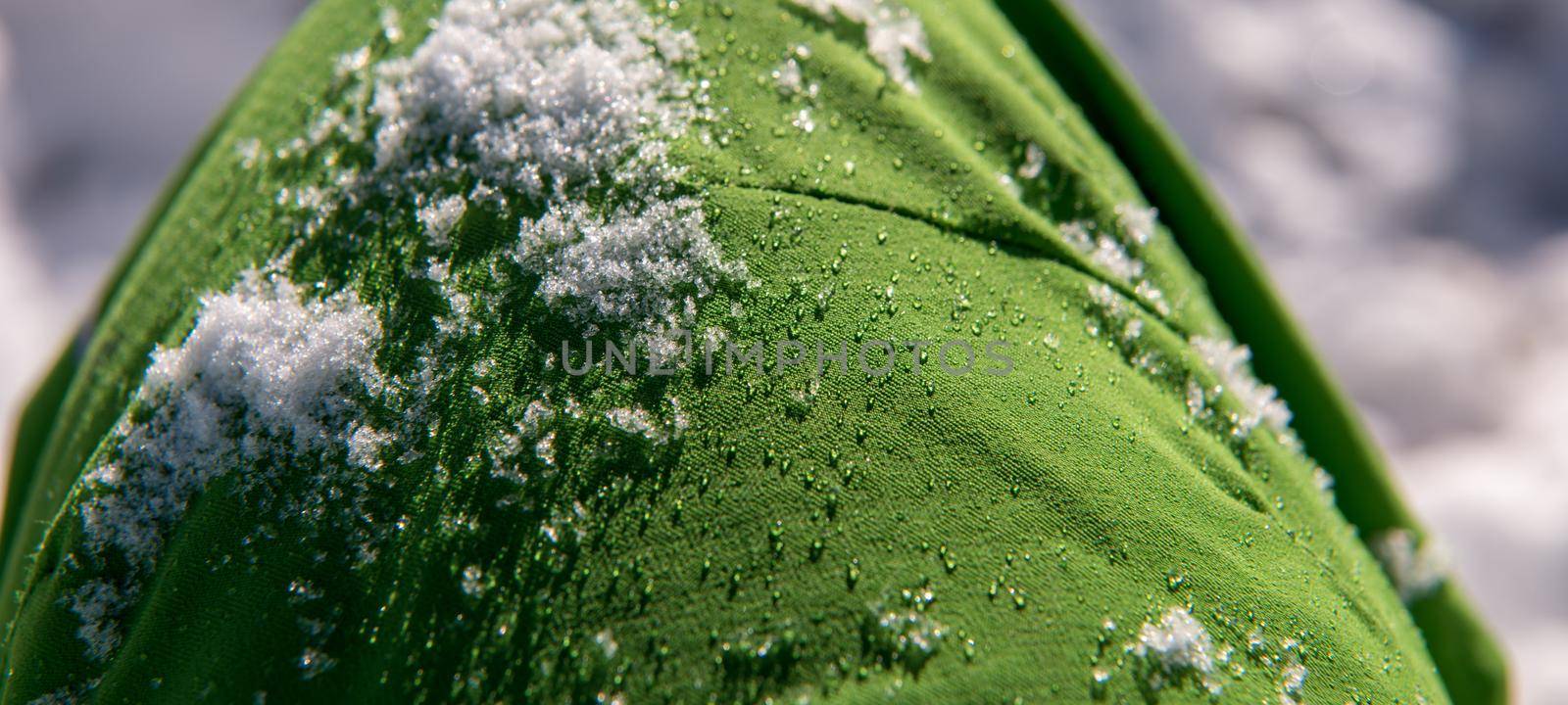 Snow and  water droplets on green waterproof fabric from skiing clothes in winter